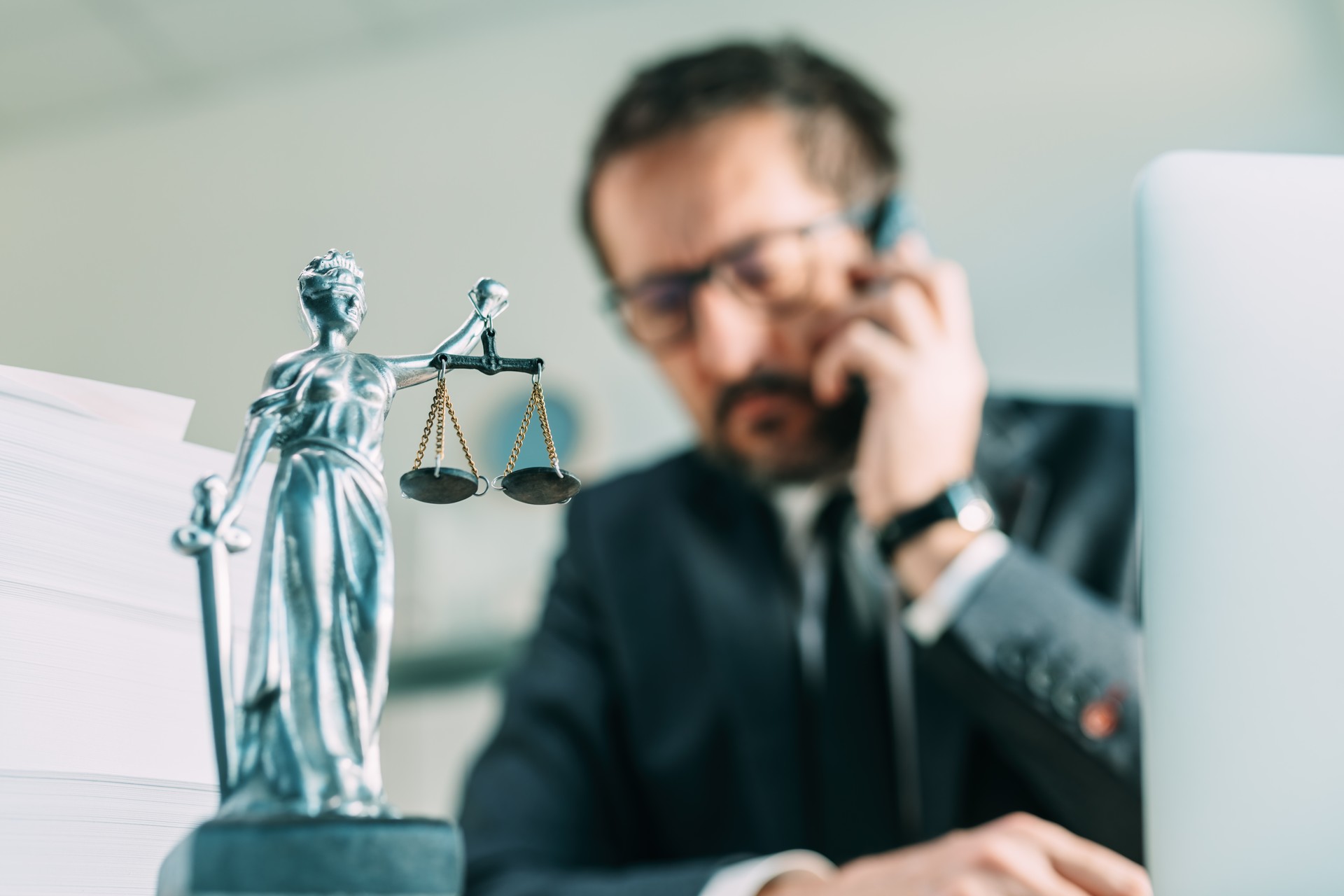 Lawyer on the phone, attorney talking on smartphone from his office with Lady Justice statue on desk